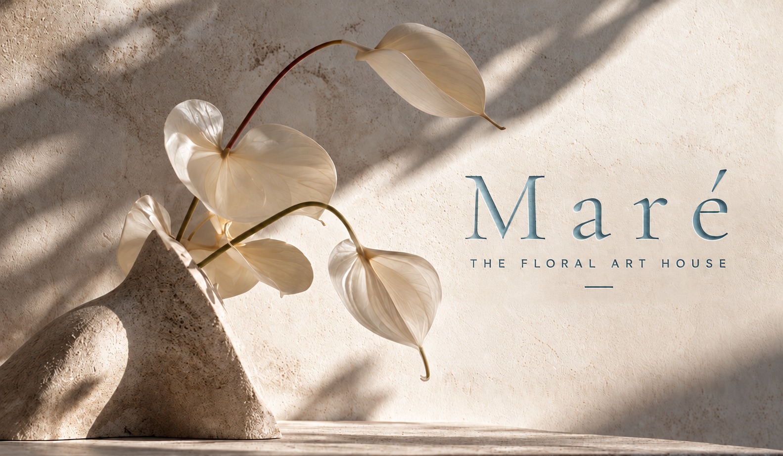 White anthuriums in a sculptural stone vase against sunlit warm plaster, with the blue Maré lettering and The Floral Art House inscription